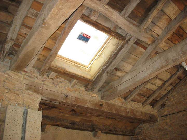 Structure de toiture traditionnelle avec poutres en bois brut et fenêtre VELUX Mâcon